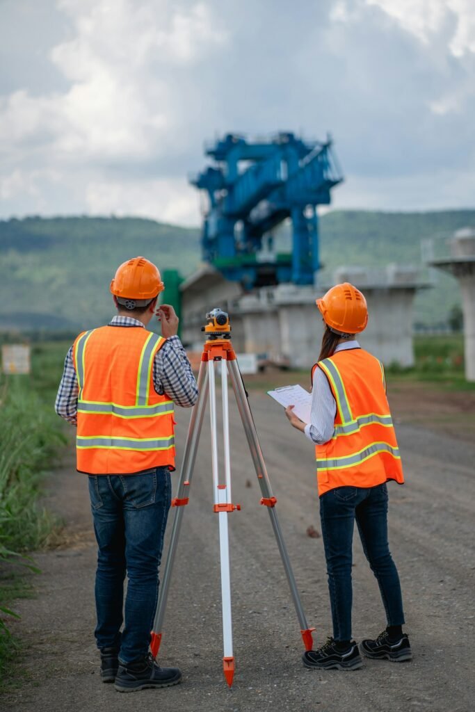 Survey team is working with a theodolite and road construction plans.